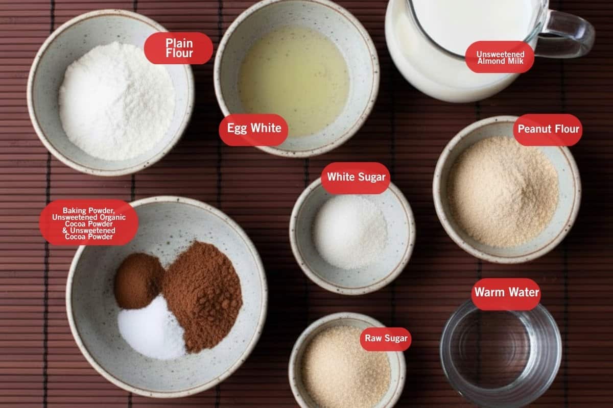 Flat lay of ingredient shot of plain flour, egg white, unsweetened almond milk, peanut flour, white sugar, warm water, baking powder, unsweetened cocoa powder, unsweetened organic cocoa powder, raw sugar - 2