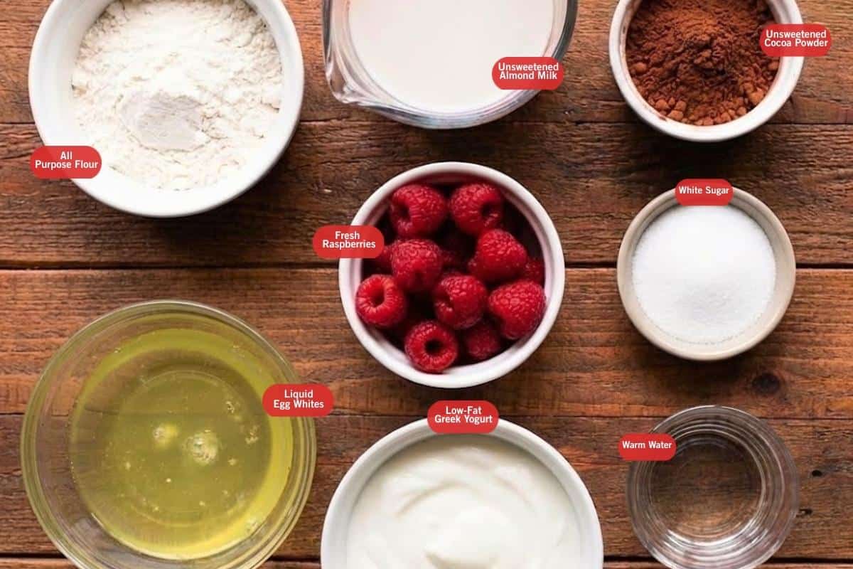 Flat lay photo of all purpose flour, unsweetened almond milk unsweetened cocoa powder, white sugar, fresh raspberries, low- fat greek yogurt, warm water, liquid egg whites - 2