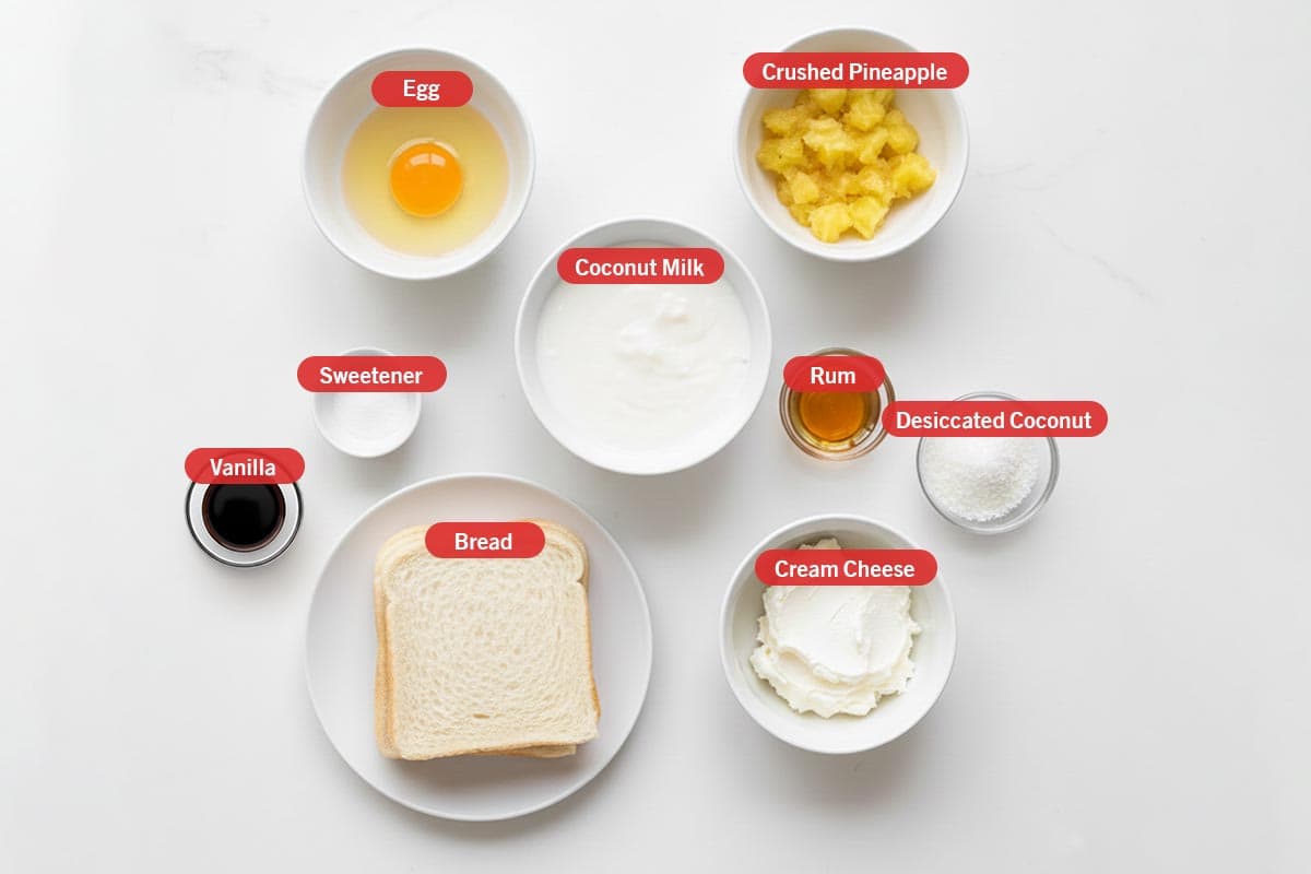 Top shot of ingredients: egg, crushed pineapple, coconut milk, rum, dessicated coconut, cream cheese, bread, sweetener, and vanilla.