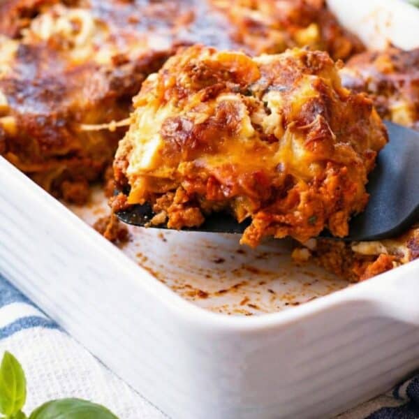 A picture of a lasagna side view with a fork lifting a slice off a baking dish