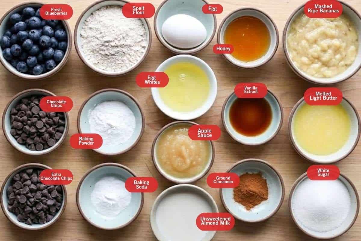 Flat lay photo of fresh blueberries, spelt flour, egg, egg whites, apple sauce, chocolate chips, extra chocolate chips, baking powder, baking soda, unsweetened almond milk , ground cinnamon, vanilla extract, honey, melted light butter, white sugar, smashed ripe bananas, vanilla extract - 2