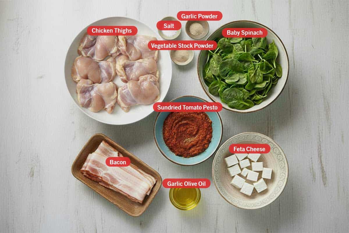Top shot of ingredients: Chicken thighs, salt, garlic powder, vegetable stock powder, baby spinach, sundried tomato pesto, bacon, garlic olive oil, and feta cheese. - 2