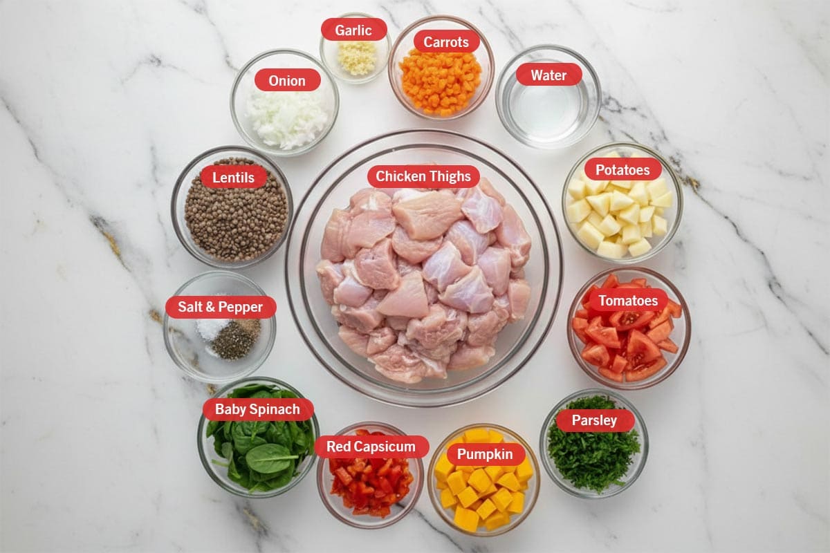 Top shot of ingredients: carrots, water, potatoes, tomatoes, parsley, pumpkin, red capsicum, baby spinach, salt & pepper, lentils, onion, garlic, and chicken thighs.