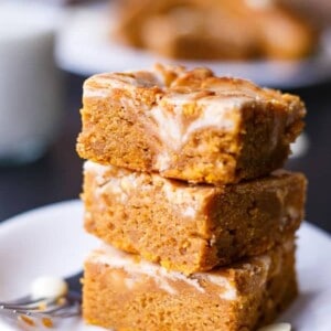 Cinnamon Cheesecake Swirl Pumpkin Bars stack on each other on a plate