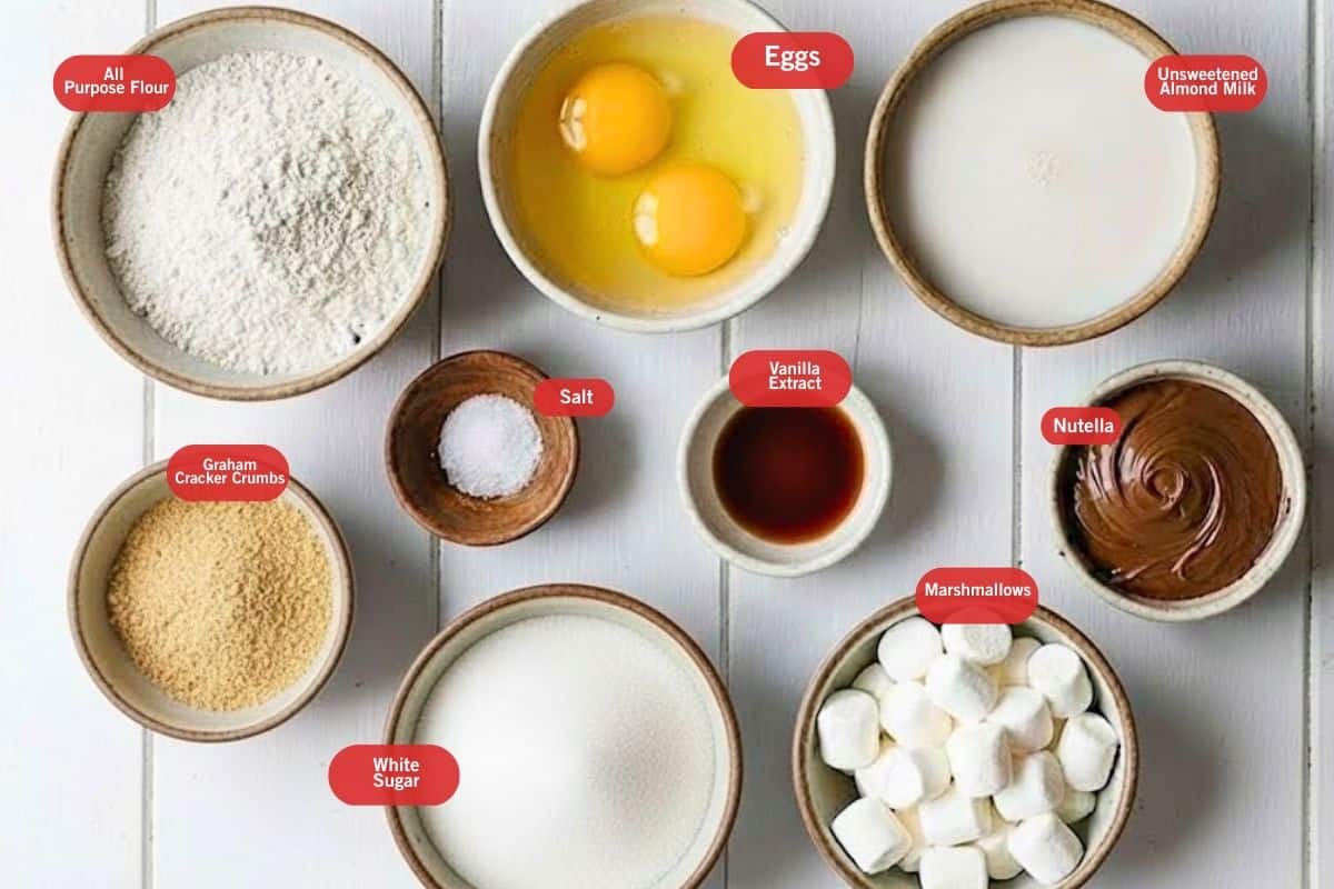Flat lay photo of ingredient shot of all purpose flour, eggs, unsweetened almond milk. nutella, vanilla extract, marshmallows, white sugar, salt, graham cracker crumbs