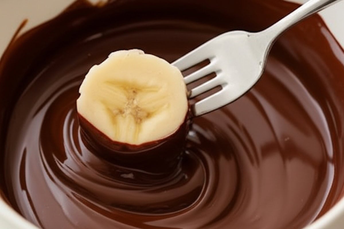 Dip one banana slice at a time into the melted chocolate.