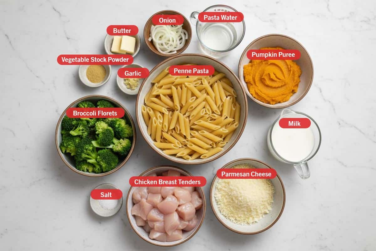 Top shot of ingredients: vegetable stock powder, garlic, butter, onion, pasta water, pumpkin puree, penne pasta, milk, parmesan cheese, chicken breast tenders, salt, and broccoli florets.
