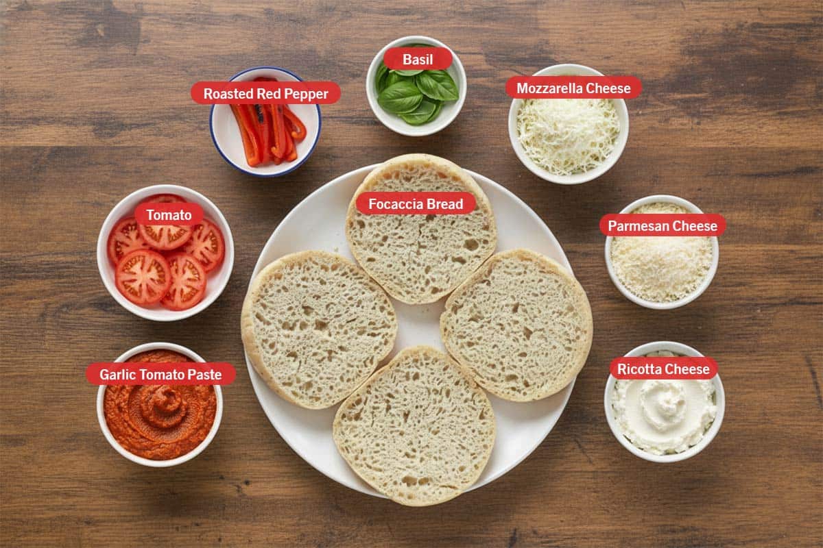 Top shot of ingredients: garlic tomato paste, tomato, roasted red pepper, basil, mozzarella cheese, parmesan cheese, ricotta cheese, and focaccia bread. - 2