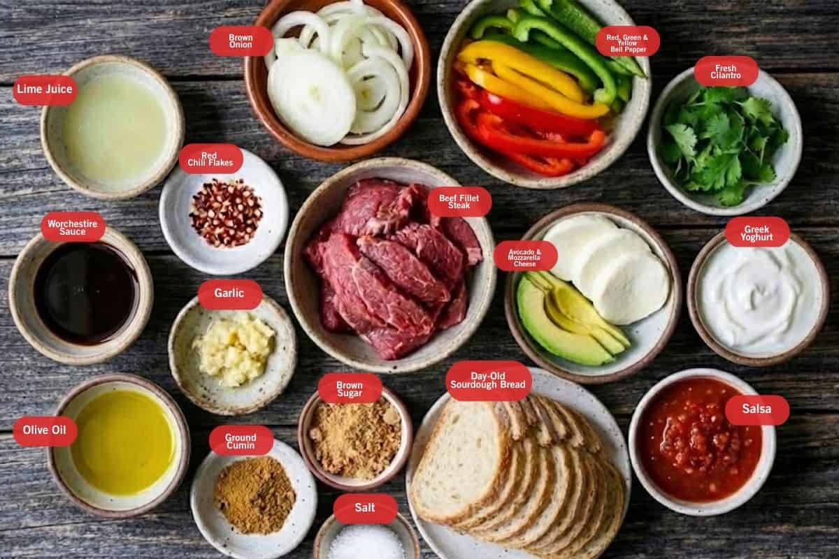 Flat lay photo of ingredient shot of lime juice, brown onion, red, green and yellow bell pepper, fresh cilantro, greek yogurt, salsa, day old sour dough bread, salt, brown sugar, garlic, beef fillet steak, olive oil, worchestire sauce, lime juice, red chili flakes, garlic, ground cumin - 2