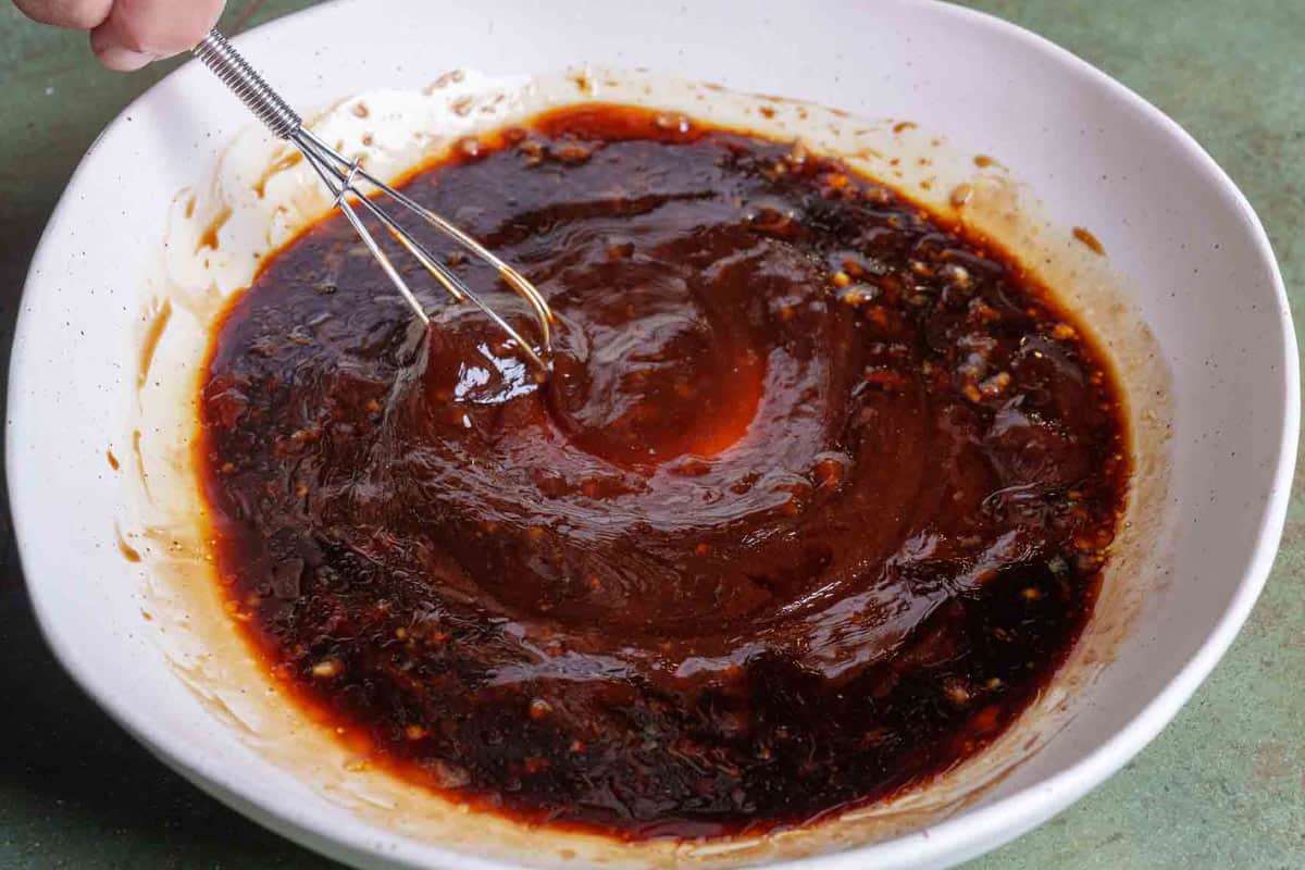 ingredients for the marinade being whisked together in a white bowl.