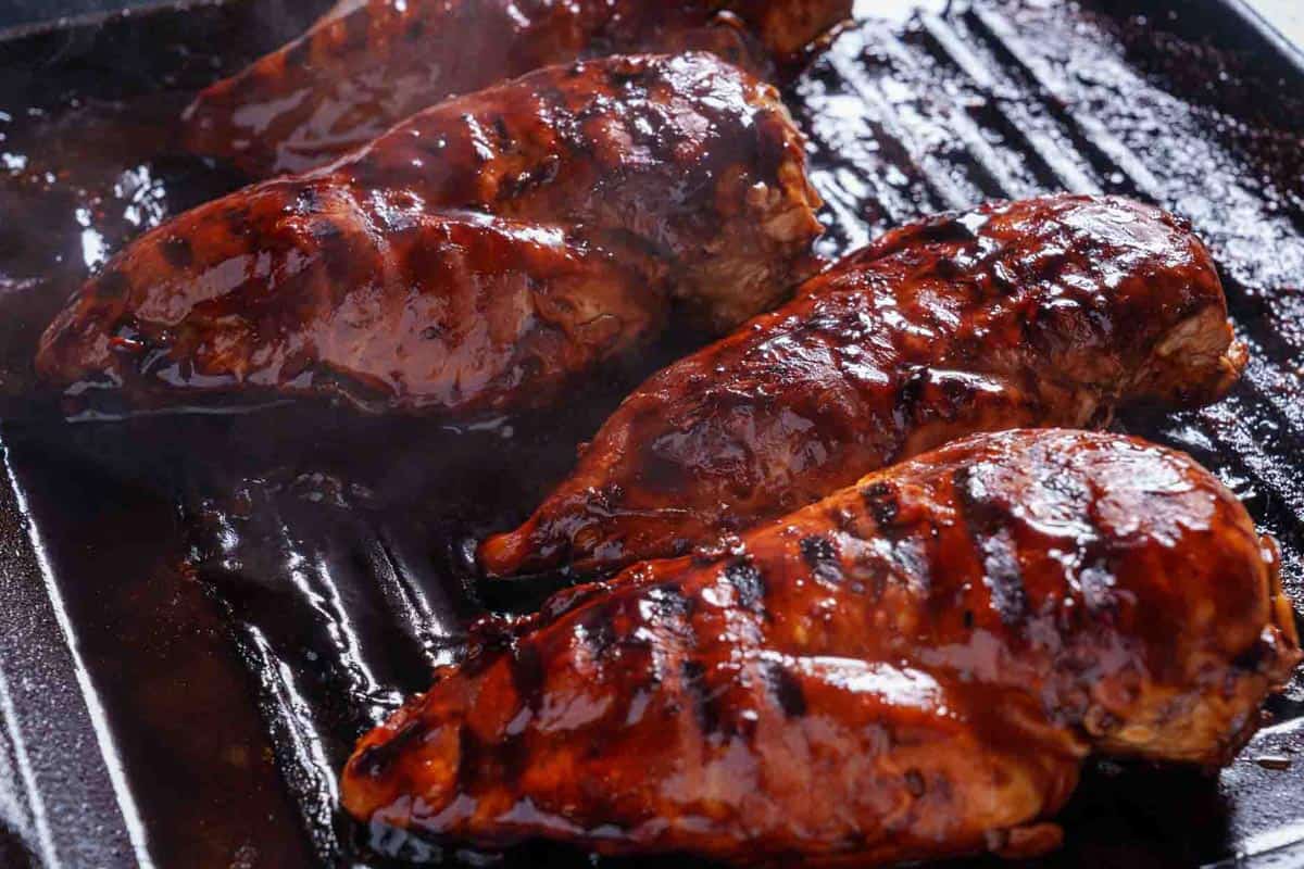 chicken breasts covered in sauce being grilled until cooked through.
