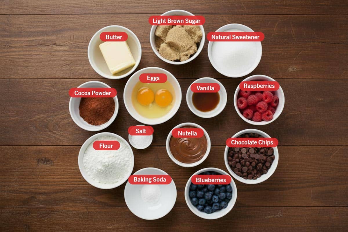 Top shot of ingredients: butter, light brown sugar, natural sweetener, raspberries, chocolate chips, blueberries, baking soda, flour, cocoa powder,eggs, vanilla, salt and nutella.