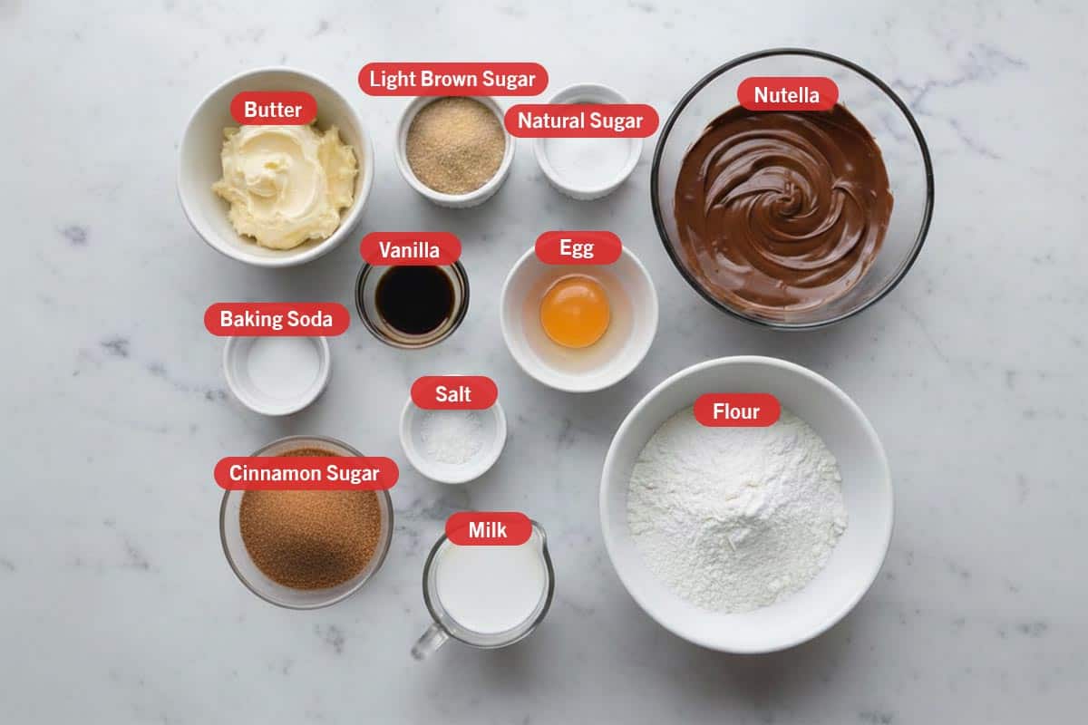 Top shot of ingredients: butter, light brown sugar, natural sugar, nutella, baking soda, vanilla, egg, cinnamon sugar, salt, milk, and flour.