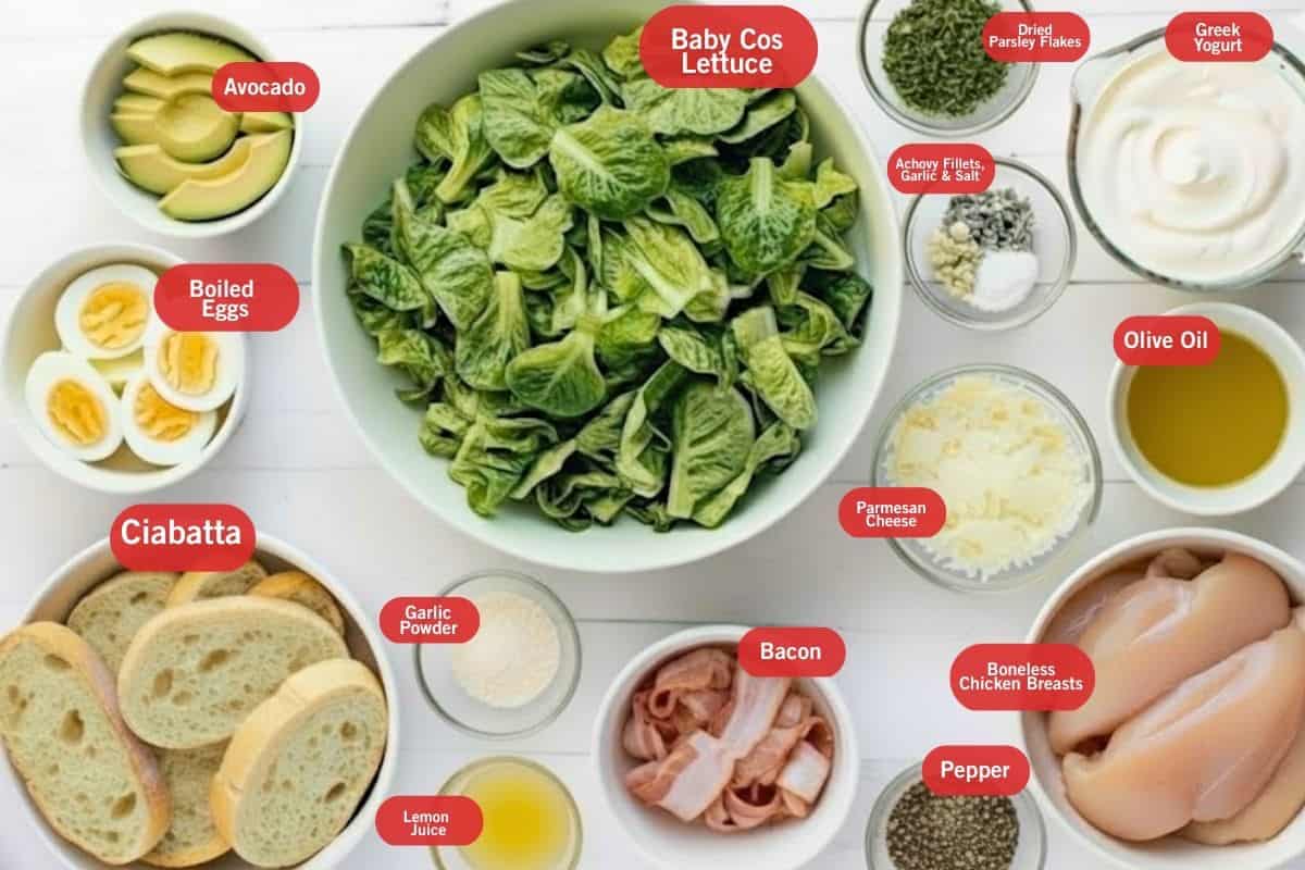 Flat lay of ingredient shot of avocado, boiled eggs, baby cos lettuce, dried parsley flakes, greek yogurt, anchovy fillets, garlic and salt, olive oil, parmesan cheese, boneless chicken breasts, pepper, bacon, ciabatta, garlic powder, lemon juice - 2