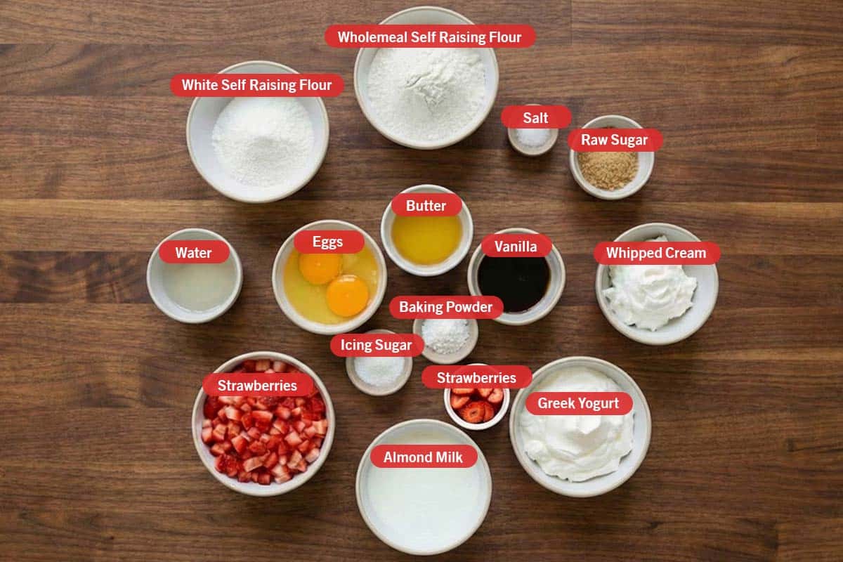 Top shot of ingredients: white self raising flour, wholemeal self raising flour, salt, raw sugar, water, eggs, butter, vanilla, whipped cream, strawberries, icing sugar, baking powder, greek yogurt, and almond milk. - 2