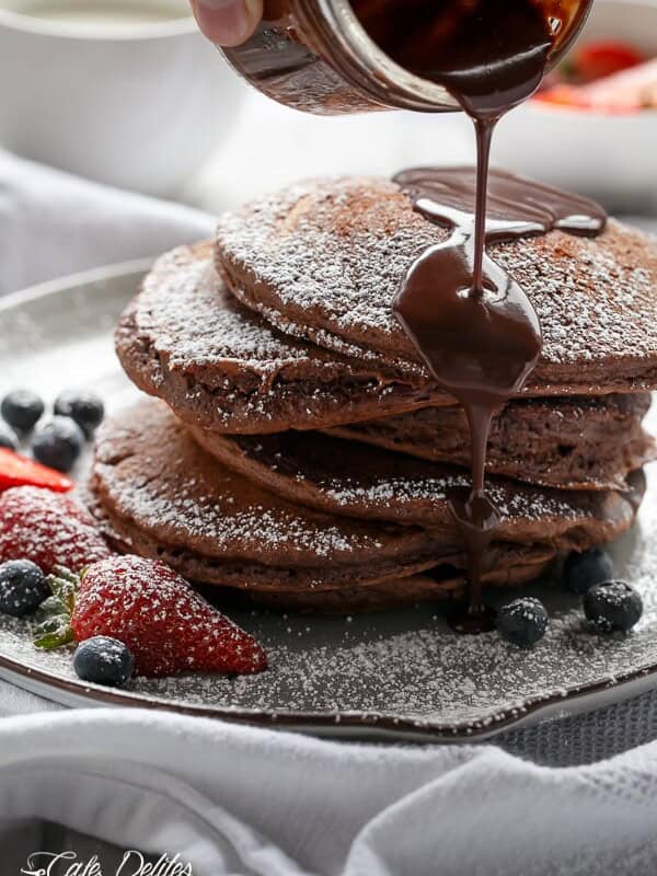 Double Chocolate Brownie Pancakes stack on each other with chocolate sauce dripping on it