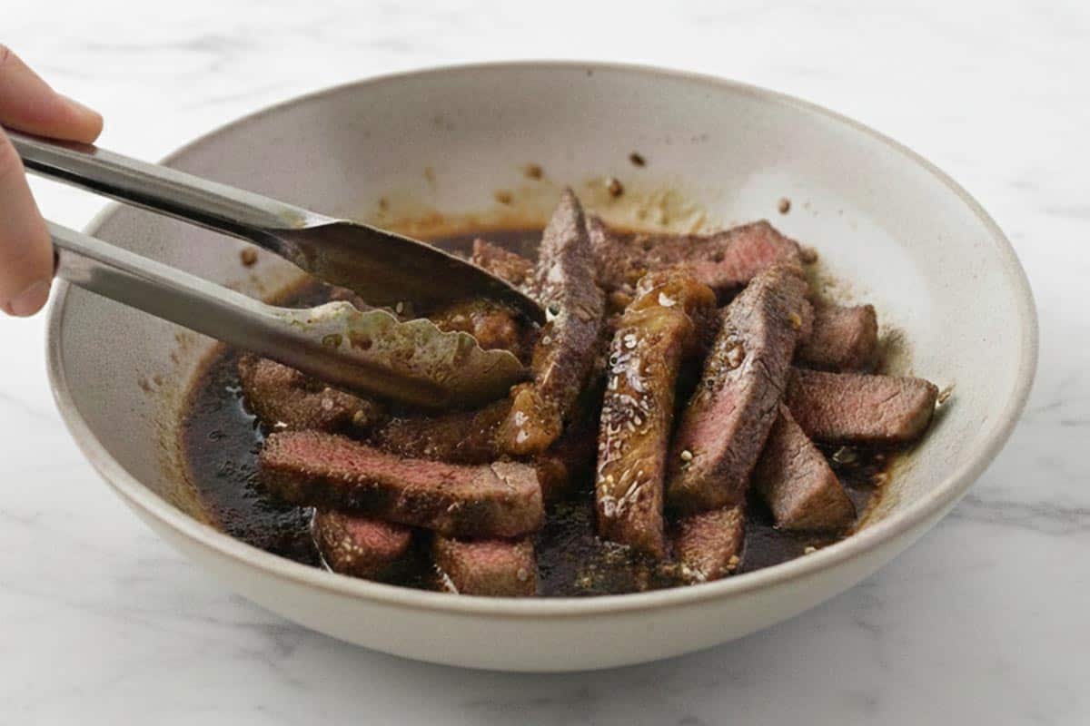 Coating the steak strips in the reduced marinade.