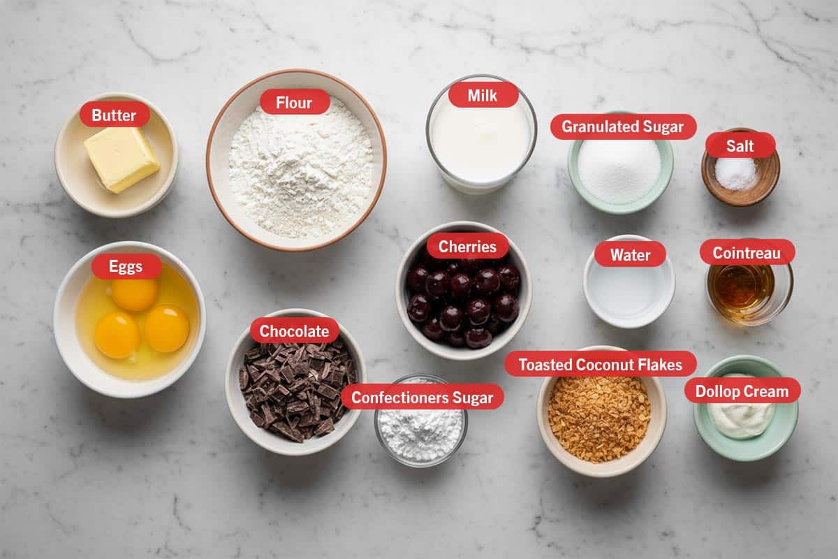 Top shot of ingredients: butter, flour, milk, granulated sugar, salt, eggs, chocolate, cherries, confectioners sugar, water, toasted coconut flakes, cointreau, and dollop cream. - 2