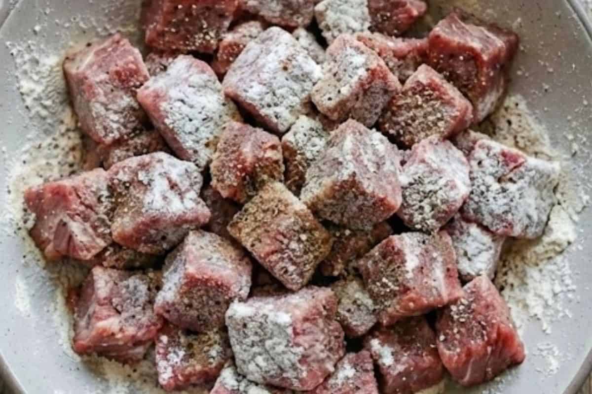 Season the diced chuck steak with salt and pepper, then toss it evenly in flour until coated. - 3