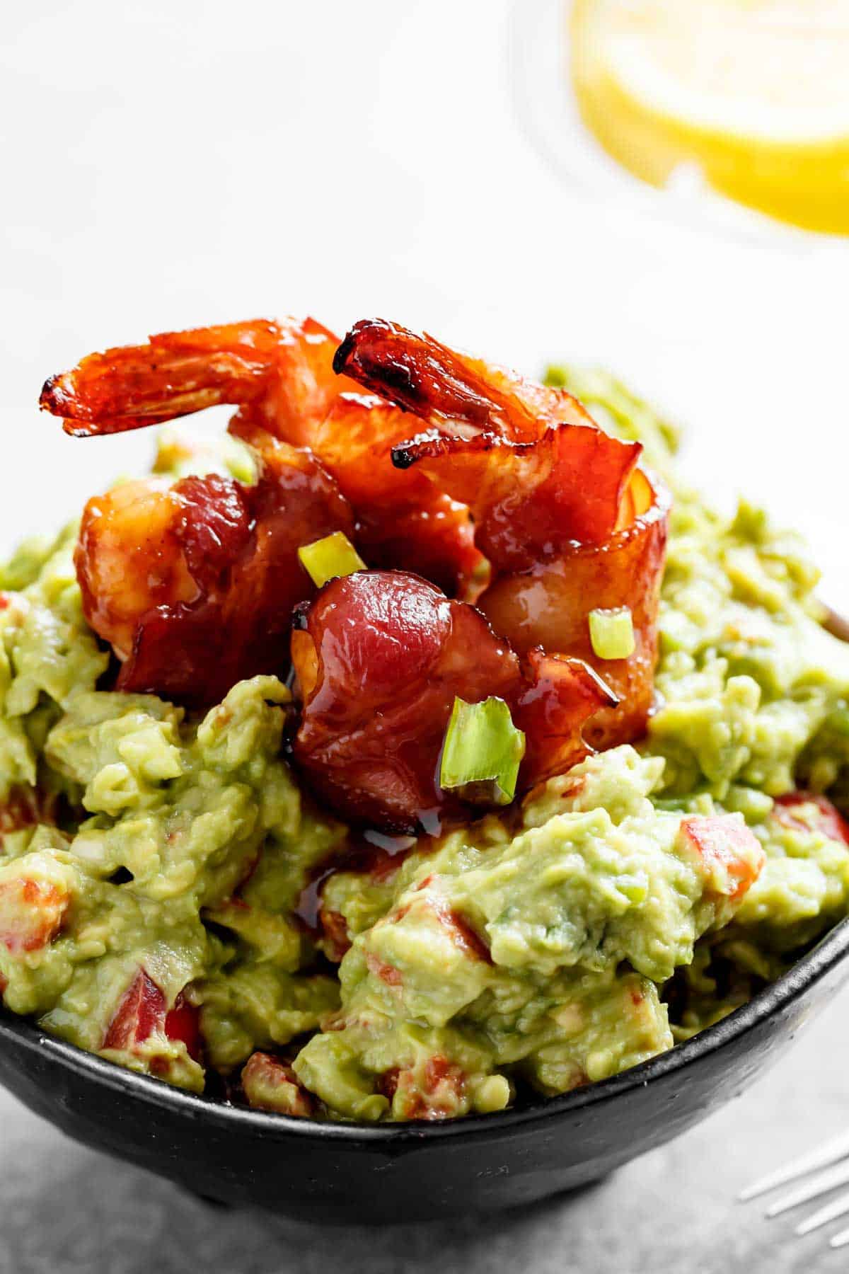 A bowl of guacamole with two glazed, wrapped prawns on top.