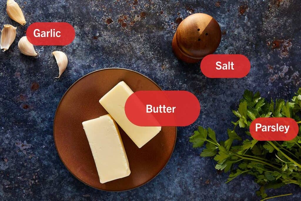 ingredients for garlic butter all on a table with a slab of butter in the middle.