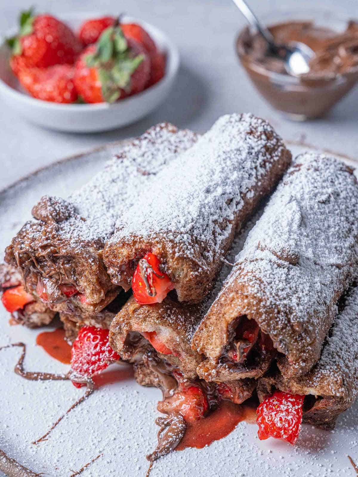 A picture of delicious French Toast Roll Ups filled with Nutella and strawberries, topped with a dusting of icing sugar.