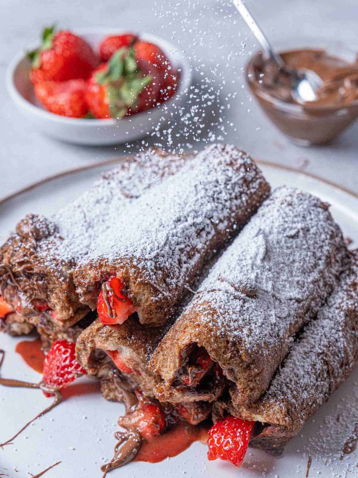 Image of the finished French toast roll-ups with icing sugar being sprinkled on top.