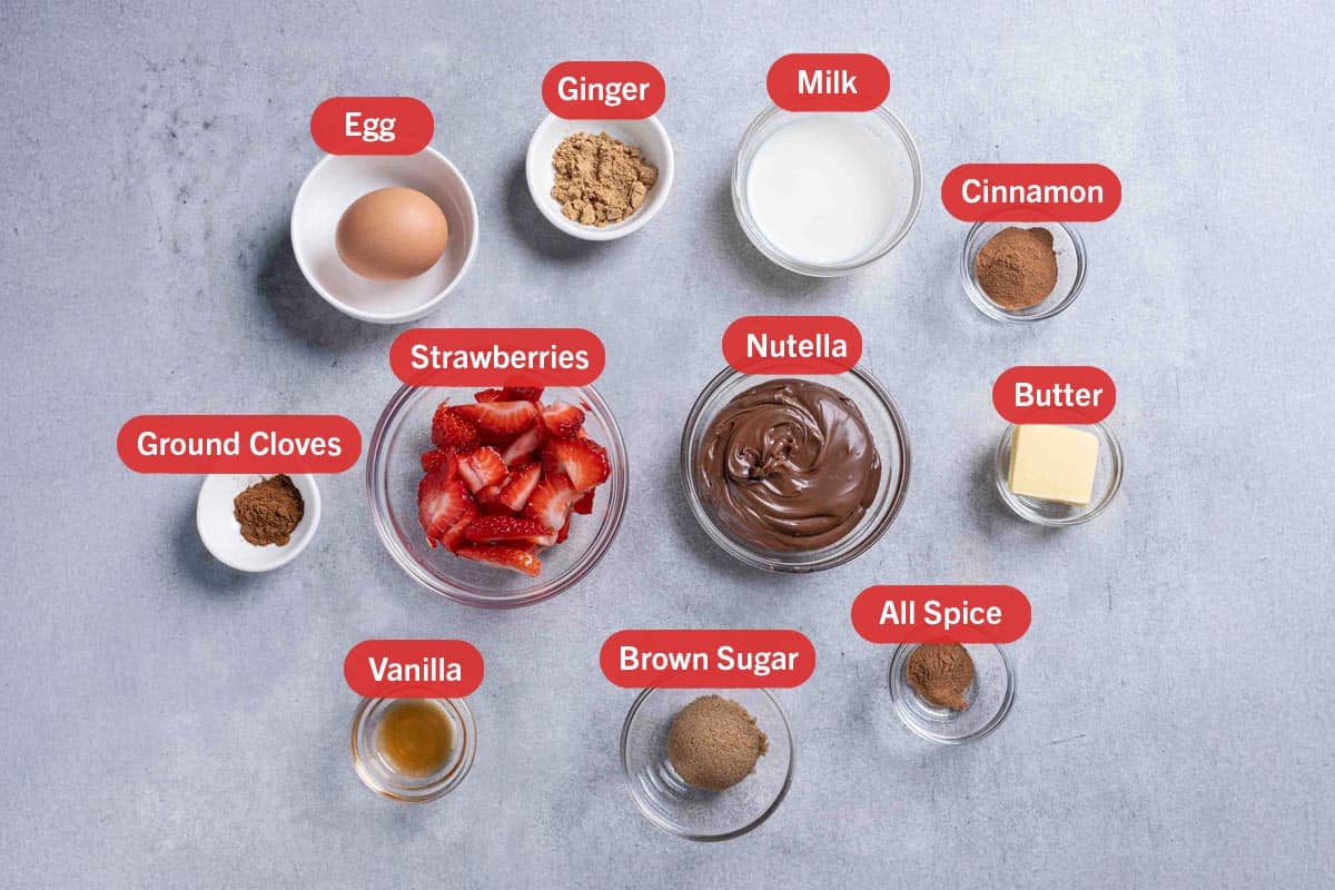 A picture of the ingredients needed to prepare the French Toast Roll-Ups, specifically: one egg, ginger, milk, cinnamon, ground cloves, strawberries, Nutella, butter, vanilla, brown sugar, and allspice.