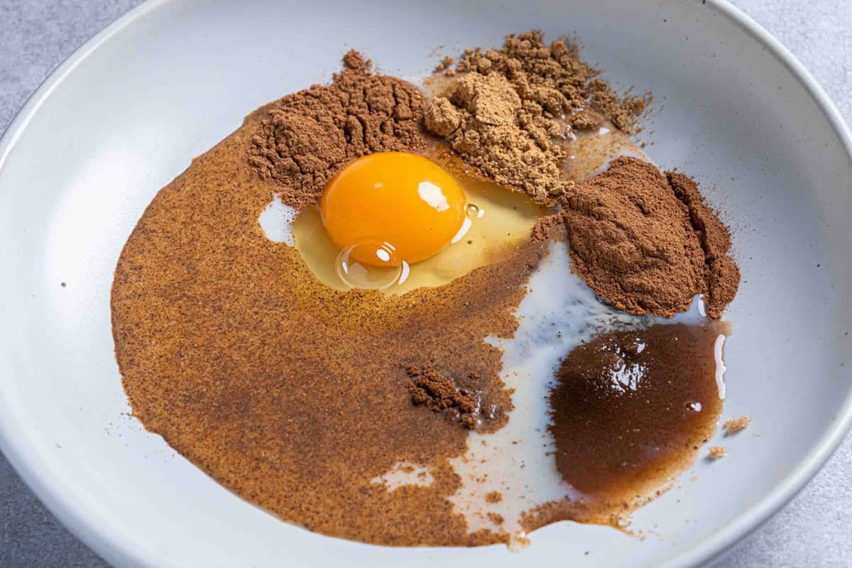 Image of ginger, cinnamon, allspice, cloves, and brown sugar in a white mixing bowl.