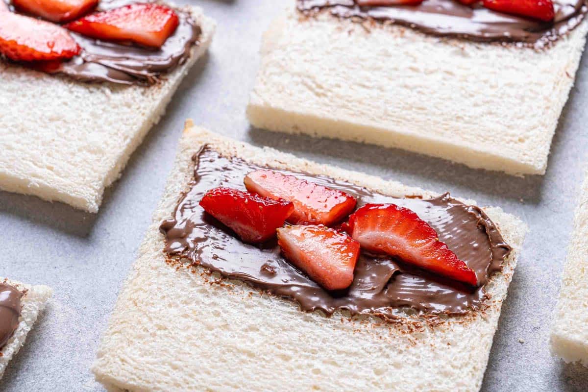 A close-up of sliced bread, half covered in Nutella and garnished with strawberries.