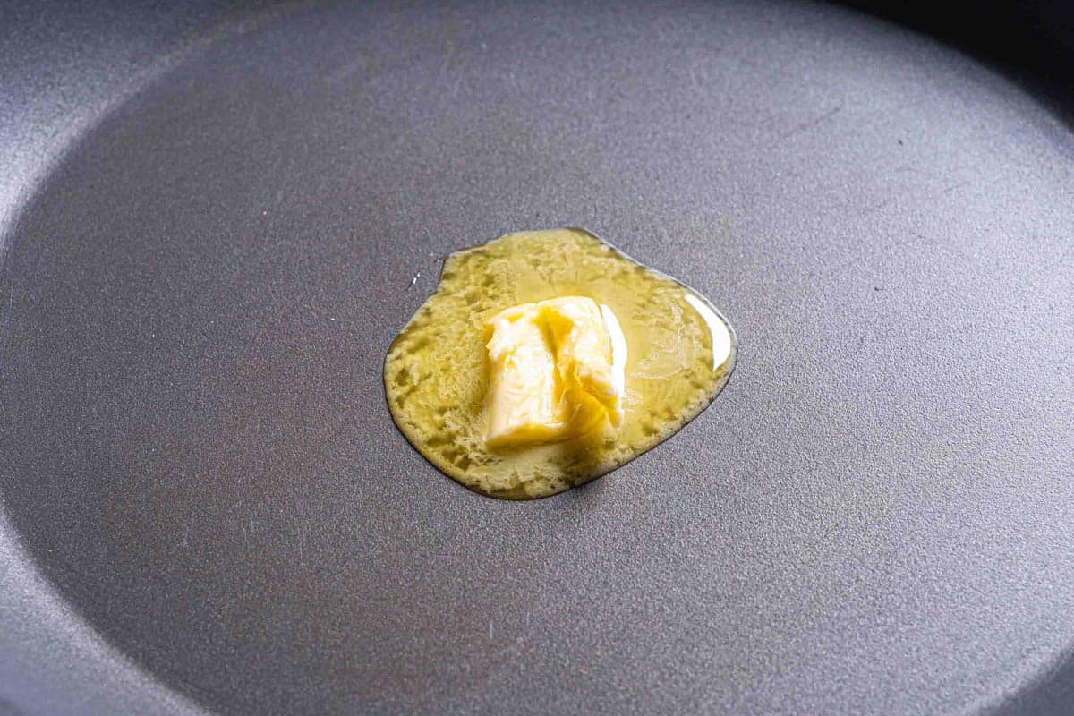 A close up image of a knob of butter melting in a skillet.