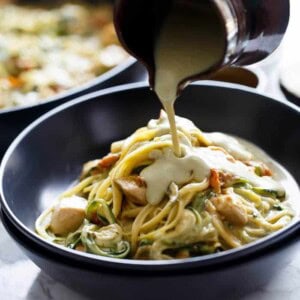 A creamy sauce pouring over Avocado Alfredo Zoodles With Chicken + Sun Dried Tomatoes