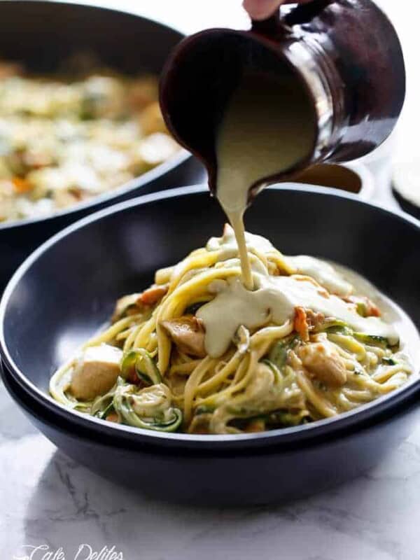 An avocado 'alfredo' sauce pouring over Avocado Alfredo Zoodles With Chicken + Sun Dried Tomatoes  in a pan