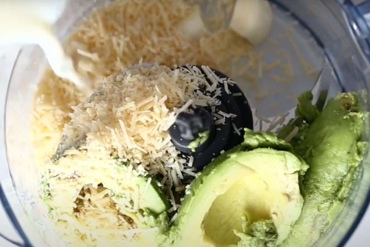Combining the avocados, garlic, parmesan, milk, salt, sun dried tomato oil, and lemon juice in a food processor.