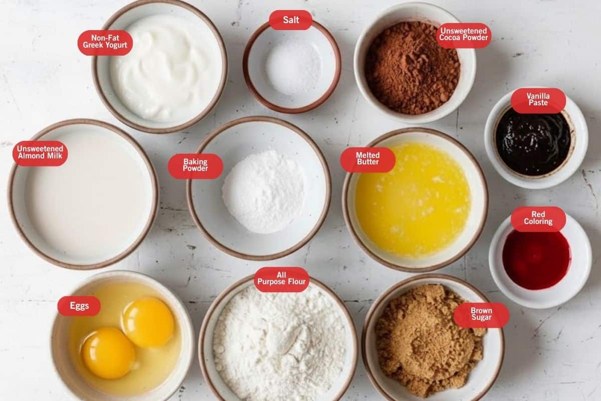 Flat lay photo of ingredient shot of non fat greek yogurt, salt, unsweetened cocoa powder, vanilla paste, red food coloring, brown sugar, all purpose. flour, eggs, melted powder, baking powder, unsweetened almond milk - 2
