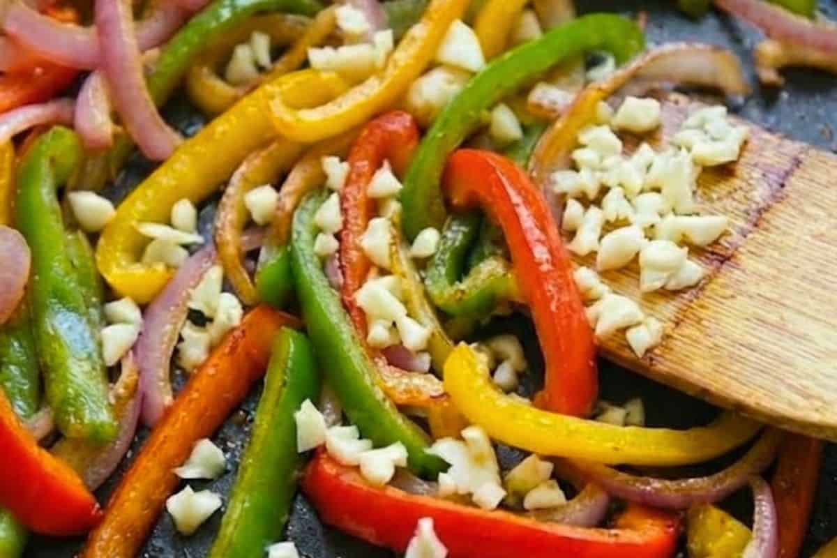 While the potatoes cook, heat olive oil in a skillet over medium-high heat. Add sliced onion and cook until soft, then toss in the garlic and bell peppers until fragrant. - 5