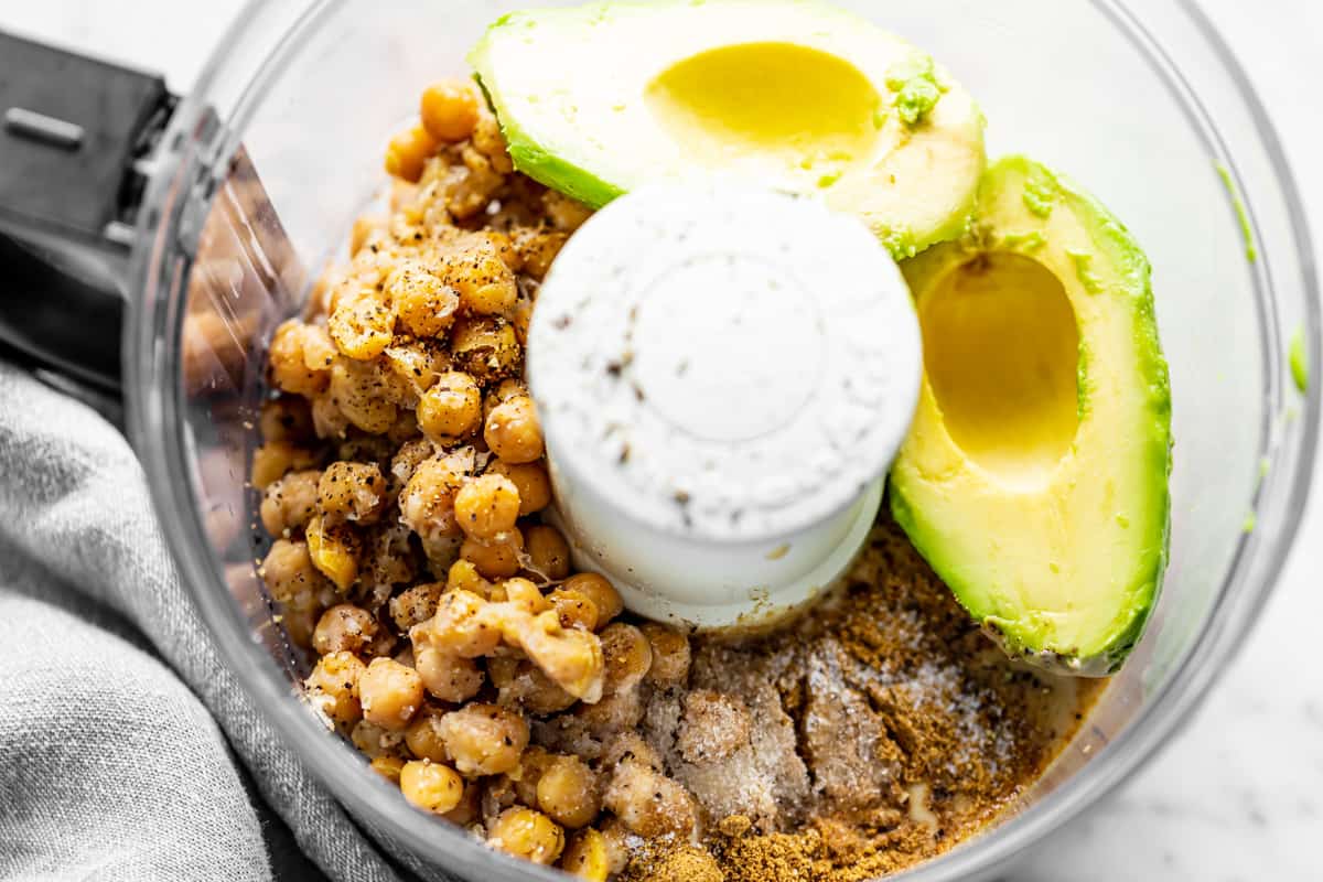 Ingredients for avocado hummus in a food processor bowl ready to be blended.