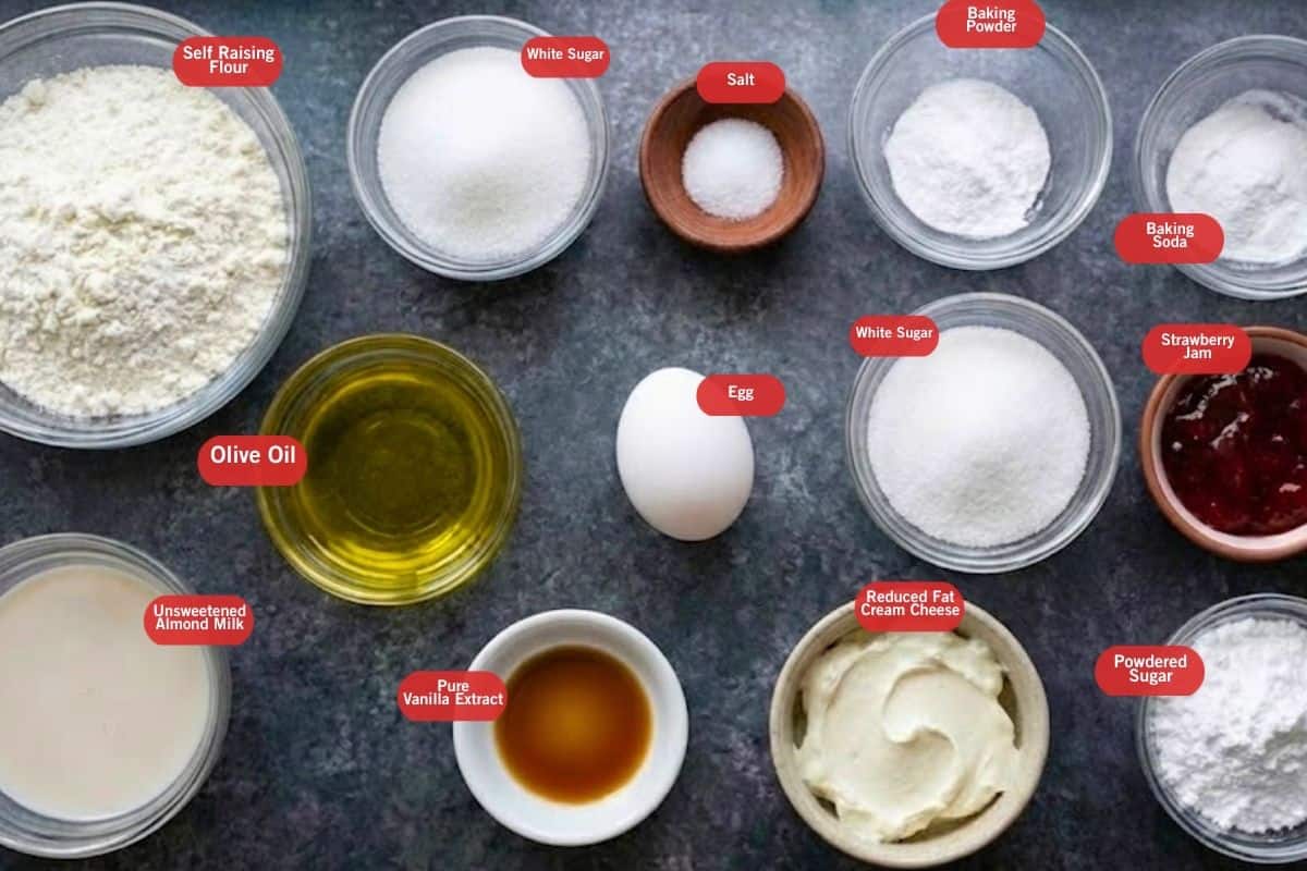 Flat lay photo of ingredient shot of self raising flour, white sugar, salt, baking powder, baking soda, strawberry jam, powdered sugar, reduced fat cream cheese, egg, pure vanilla extract, unsweetened almond milk, olive oil. - 2