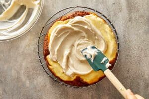 Cream cheese mix being spread into a baked carrot cake cheesecake