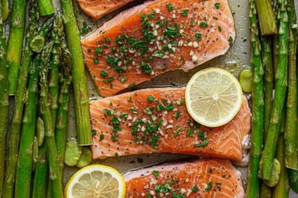 Salmon fillets with lemon slices, and asparagus and green around in one layer.