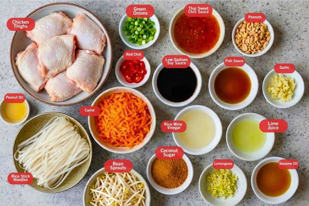 Flat lay photo of ingredient shot of chicken thighs green onions, peanut oil, red chili, peanuts, thai sweet chili sauce, low sodium soy sauce, fish sauce, garlic, lime juice, sesame oil, rice wine vinegar, lemongrass, coconut sugar, bean sprouts, carrot, rice stick noodles