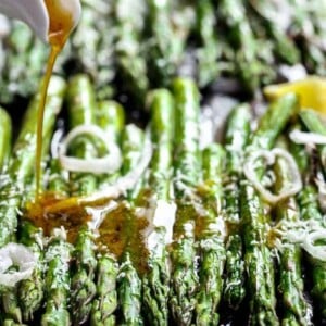 A dressing pouring over Garlic Browned Butter Baked Asparagus with Parmesan Cheese