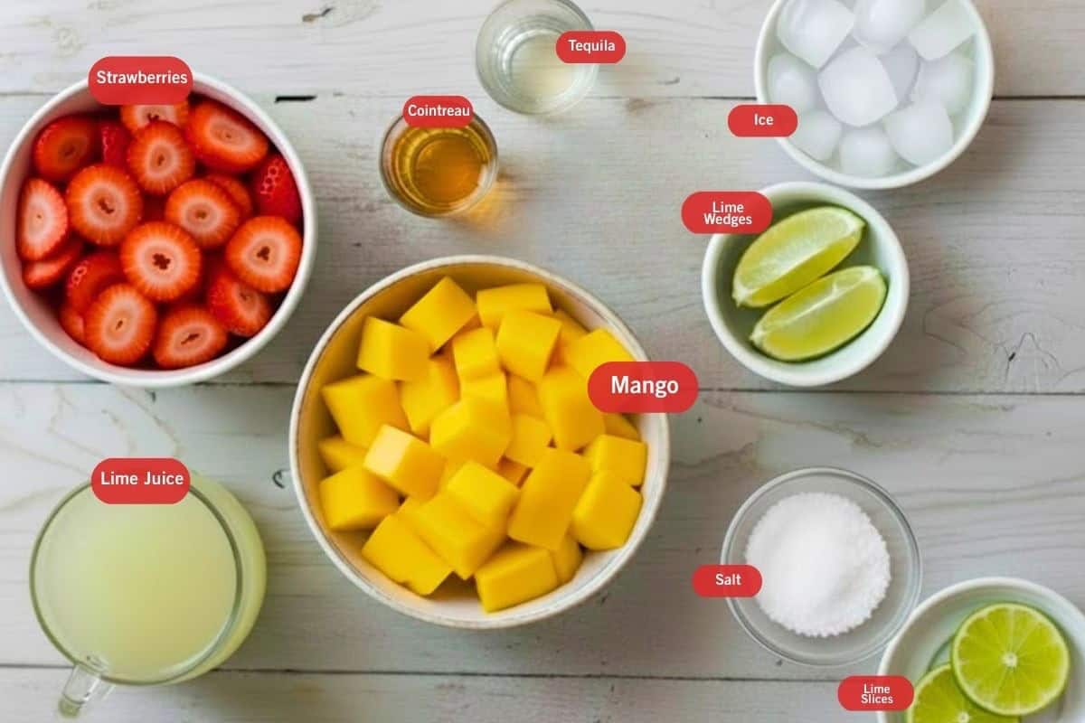 Flat lay photo of strawberries, tequila, cointreau, ice, lime wedges, mango, salt, lime slices, lime juice