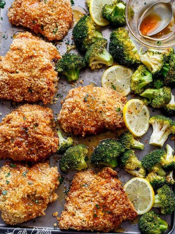 The image shows six breaded chicken breasts laid out on a metal baking sheet, surrounded by florets of broccoli and slices of lemon. The chicken breasts are golden brown and appear to be cooked to perfection. The broccoli florets are vibrant green, indicating freshness. The lemon slices, with their bright yellow color, add a refreshing contrast to the image.