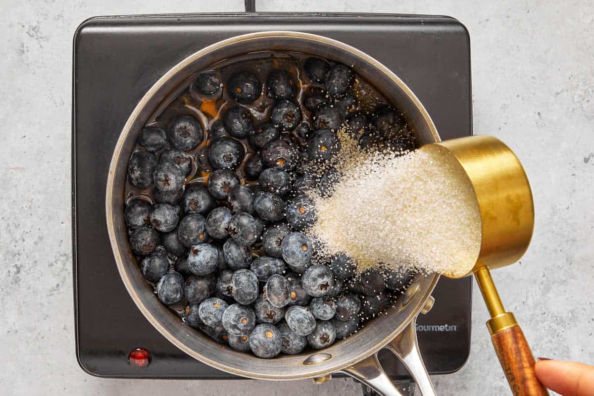 adding sugar on a pot with blueberries