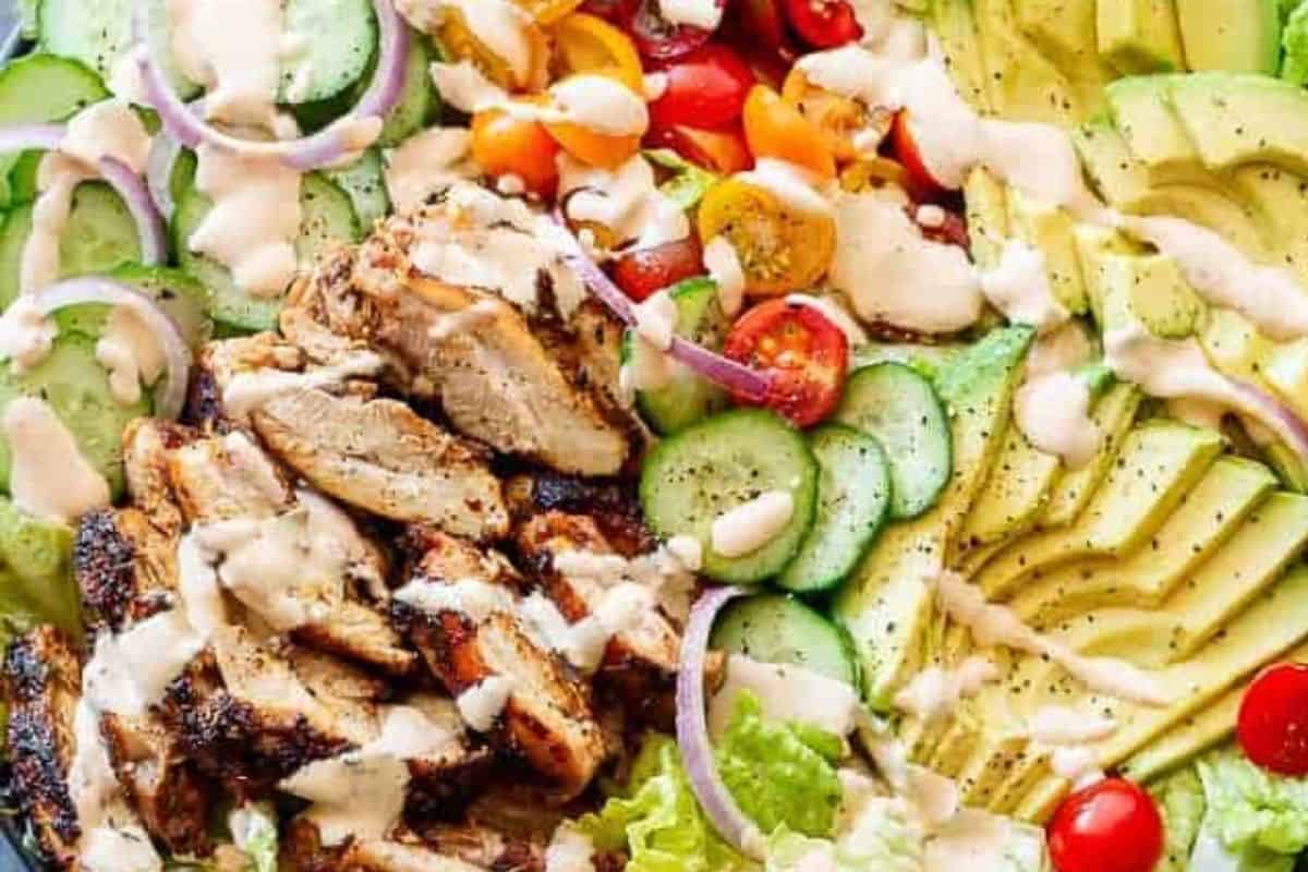 Arrange the lettuce, cucumber, tomatoes, avocado, and red onion on a serving plate. Slice the grilled chicken into strips and place them neatly on top of the salad.