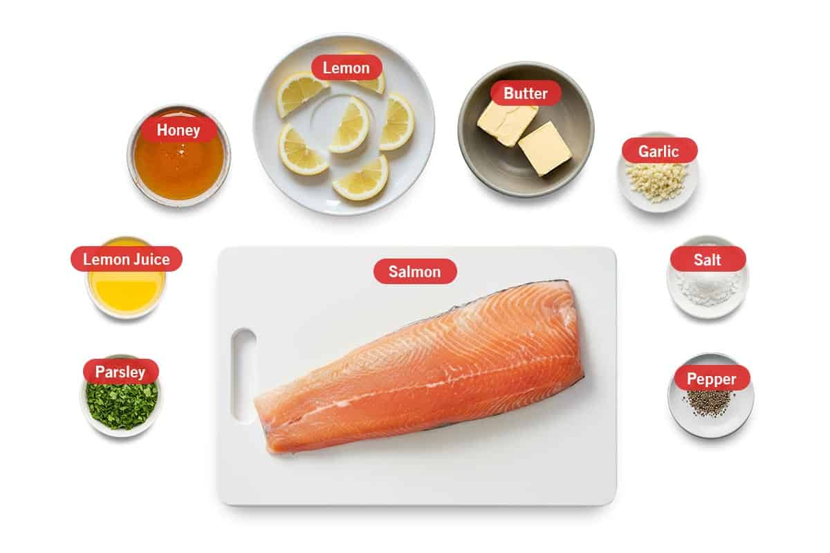 Top shot of ingredients: Parsley, lemon juice, honey, lemon, butter, garlic, salt, pepper, and salmon.