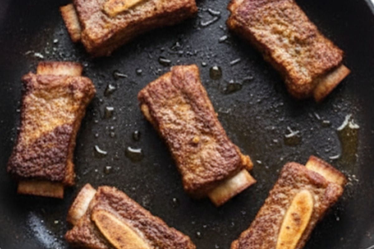 rim excess fat from the short ribs, then heat oil in a skillet over medium-high. Brown the ribs in batches for 3–4 minutes per side until golden.