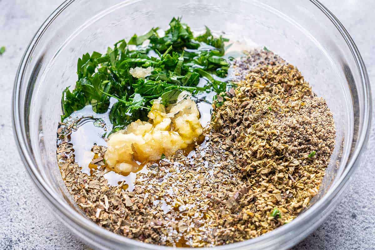 mixing bowel with minced garlic, herbs, olive oil, lemon juice, seasonings and vinegar.