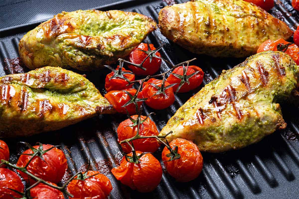 cooked pesto chicken on a grille plate with tomato and sear lines